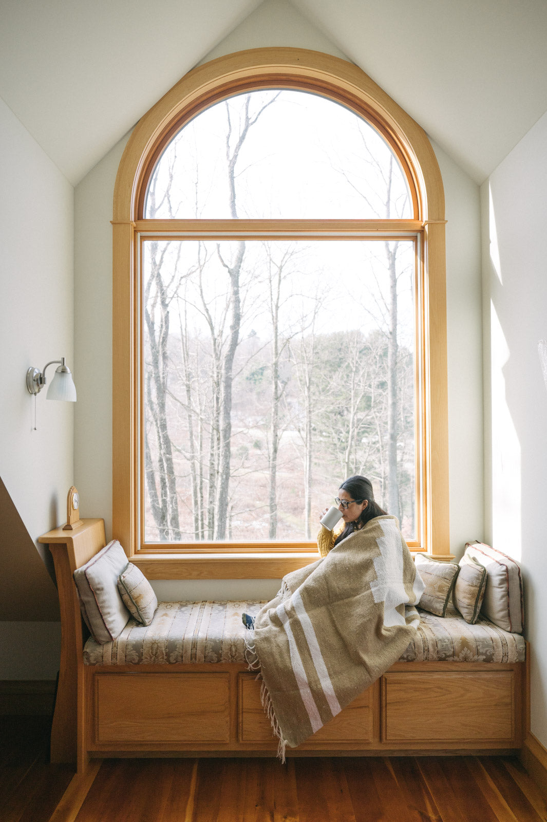 Woman wearing tan mexican blanket in window reading nook