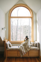 Woman wearing tan mexican blanket in window reading nook